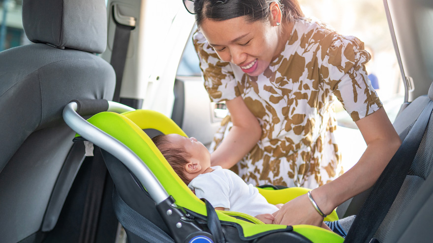 Mother placing little newborn baby boy son in a car seat baby carrier in a car