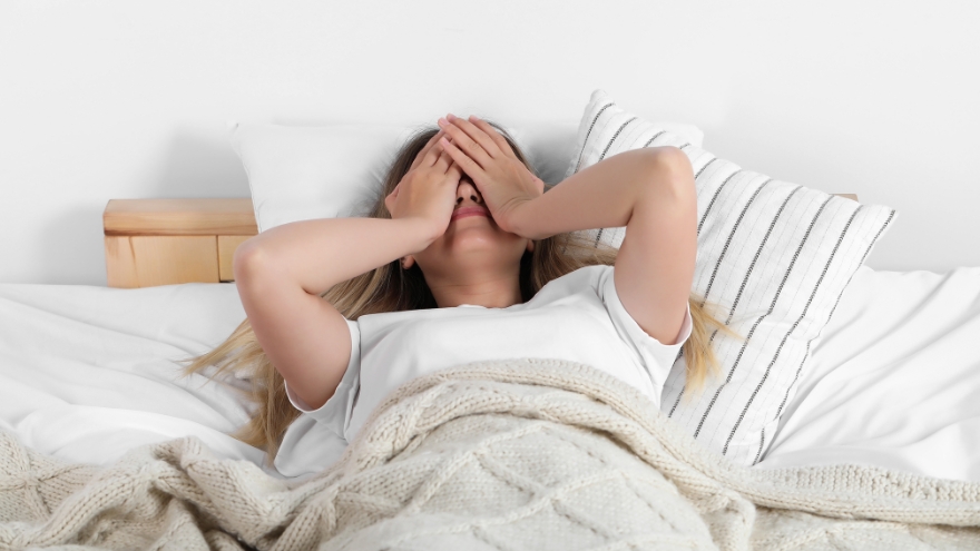 A woman in bed puts her hands over her face in exhaustion.