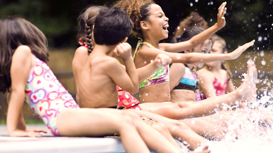 Group of kids sitting on edge of pool, splashing