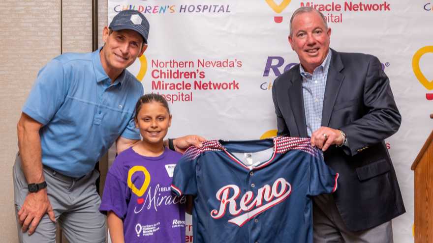 Steve Young holds up Reno jersey with Emmalee Sutton (Children's Miracle Network Hospitals) and Greg Walaitis (Renown Health).